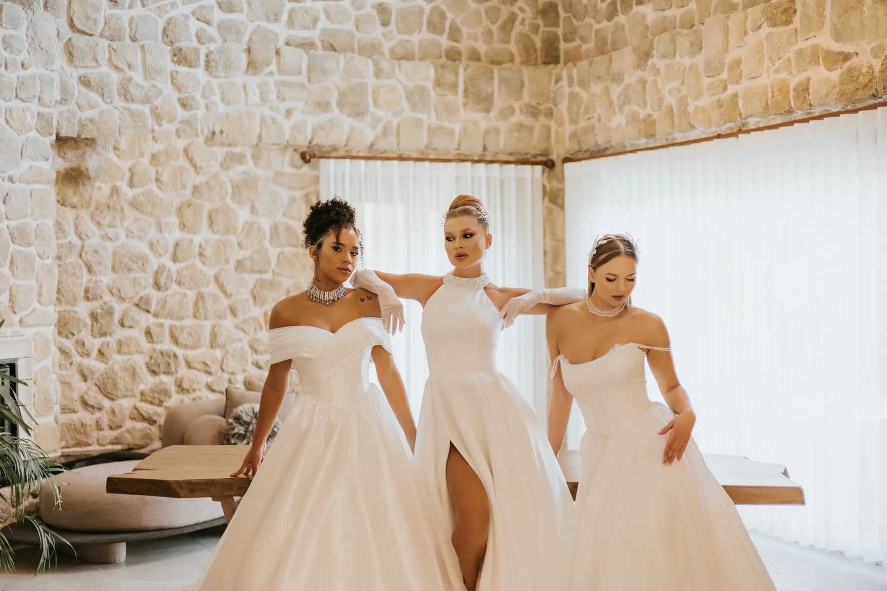 Henna Bride koleksiyonu: Taş duvarlı salonda üç model yan yana; hacimli etekler ve inci detaylar.